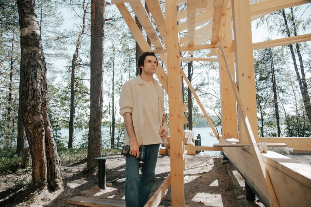 Carpenter working on wooden house frame outdoors, by a lake.