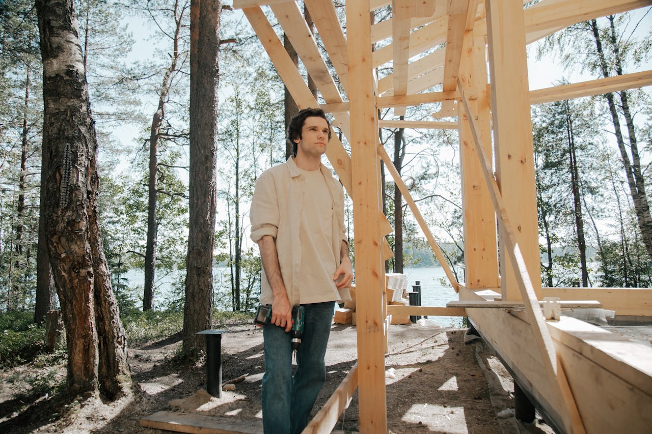Carpenter working on wooden house frame outdoors, by a lake.
